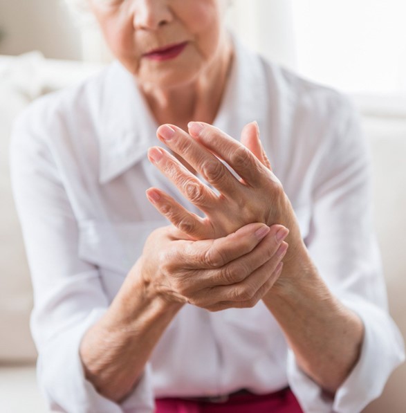 Foto de adulta tomándose una mano con la otra adolorida, en señal de Artritis Reumatoidea